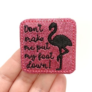 May include: Pink glitter iron-on patch with black embroidery of a flamingo and the text "Don't make me put my foot down!"