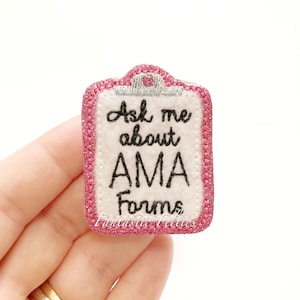 May include: Pink glitter felt patch with a white felt clipboard design. The clipboard has a silver clip and the text "Ask me about AMA Forms" is embroidered in black.