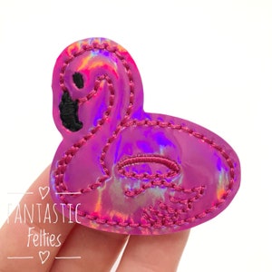 May include: A pink flamingo-shaped felt applique with a holographic finish. The flamingo has black detailing and is outlined with pink stitching. The text "Fantastic Felties" is in the lower left corner.