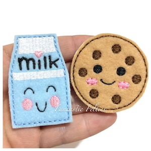 May include: Two felt appliques, a blue milk carton with the word "milk" and a brown chocolate chip cookie. Both appliques have smiling faces with pink cheeks.