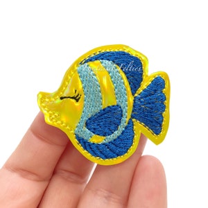 May include: A yellow and blue embroidered iron-on patch of a cartoon fish with a single eye.
