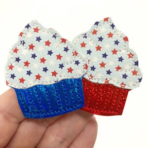 May include: Two cupcake-shaped felt appliques with a red, white, and blue star pattern. The cupcakes have a blue and red glitter finish.