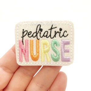 May include: A white felt patch with a rainbow embroidered word "NURSE" and the word "pediatric" in black above it.