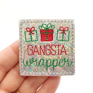 May include: A silver glitter iron-on patch with green and red embroidery of three presents and the text "Gangsta Wrapper".