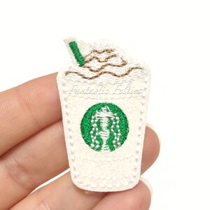May include: White felt embroidered patch of a coffee cup with whipped cream and a straw. The cup has a green logo with a white siren. The text "Fantastic Felties" is embroidered on the cup.