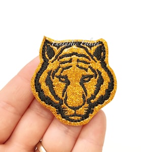 May include: A gold glitter tiger head patch with black embroidered details. The patch features the text "Fantastic Felltles" in the upper left corner. This patch is suitable for clothing, bags, or other craft projects.