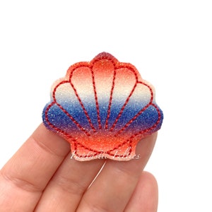 May include: A glittery seashell applique in shades of red, white, and blue, with red stitching outlining the shape. The text "Fantastic Felties" is printed in a cursive font at the bottom of the applique.