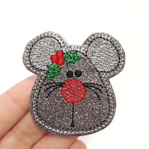 May include: A glittery gray mouse-shaped applique with a red nose, black eyes, and whiskers. The mouse has a sprig of holly with red berries and green leaves. The applique is likely for a Christmas or holiday-themed craft project.