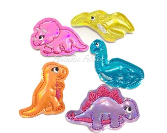 May include: Five colorful iron-on patches featuring different dinosaurs. The patches are made of iridescent fabric and have a shiny finish. The dinosaurs include a triceratops, a stegosaurus, a brachiosaurus, a pterodactyl, and a tyrannosaurus rex.