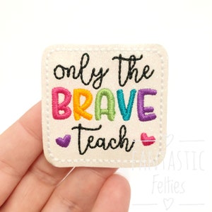 May include: A white felt patch with a rainbow embroidered message that reads "only the brave teach" with two small pink hearts on either side of the word "teach".