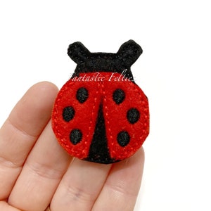 May include: A red and black felt ladybug with black dots. The ladybug is about 2 inches in diameter.