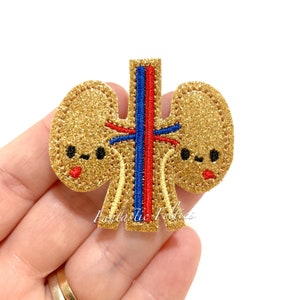 May include: Gold glitter felt applique of a pair of kidneys with a red and blue vein design. The kidneys have cute cartoon faces with black eyes and red mouths.
