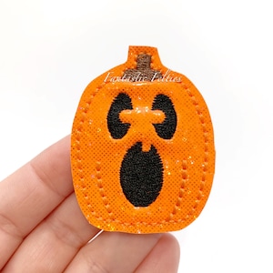 May include: Orange felt pumpkin with a surprised face and a brown stem. The pumpkin has a glittery texture and is stitched around the edges. The text "Fantastic Felties" is visible on the pumpkin. A Halloween-themed craft item.