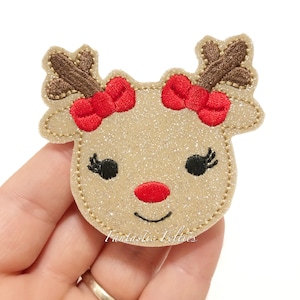 May include: A sparkly gold glitter reindeer head with red bows and a red nose. The reindeer has black eyes with eyelashes.