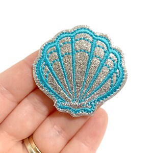 May include: A silver glitter seashell with a turquoise blue outline. The seashell is a popular design for crafts and decorations.
