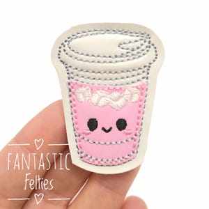 May include: A pink felt coffee cup patch with a smiling face and white whipped cream detail. The patch is outlined with gray stitching and has the text "FANTASTIC Felties".