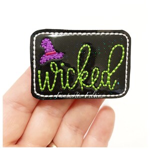 May include: Black felt patch with green glitter and a green embroidered witch hat and the word "wicked" in green embroidery. The patch has a white stitched border.