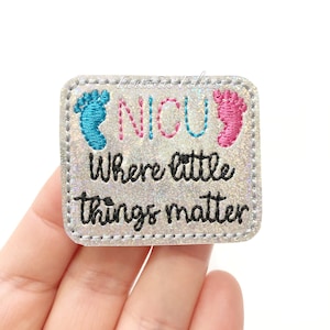 May include: A silver glitter iron-on patch with blue and pink footprints and the text "NICU Where little things matter".