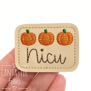 May include: A beige felt patch with three orange embroidered pumpkins and the word "nicu" in brown embroidery.