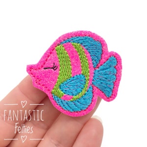 May include: A pink felt fish with green and blue stripes and a blue tail fin. The fish has a small, black eye and a white mouth.