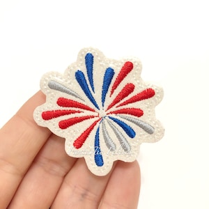 May include: A white felt patch with a red, white, and blue embroidered firework design. The patch is covered in small white glitter.