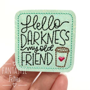 May include: A square, mint-green felt patch with the embroidered phrase "Hello Darkness My Old Friend" in black script. A brown coffee cup with a pink heart is on the bottom right. The patch has a glittery border and the words "Fantastic Felties" in the bottom left.