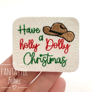 May include: White felt applique with green and red embroidery that reads "Have a holly dolly Christmas" with a brown felt cowboy hat above the text.