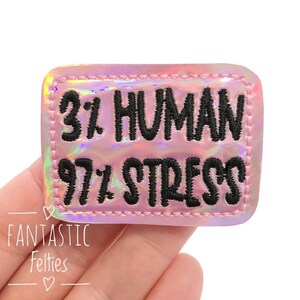 May include: A pink iridescent iron-on patch with black embroidery that reads "3% Human 97% Stress".