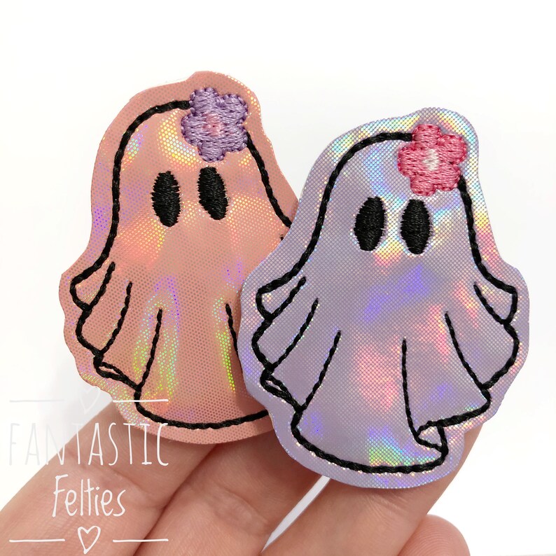 May include: Two iridescent felt ghost ornaments with black embroidered eyes and a pink and purple flower on top.
