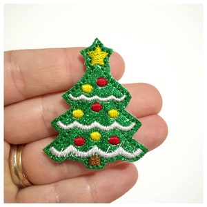 May include: A green glitter Christmas tree patch with a yellow star on top. The tree is decorated with red and yellow ornaments and white trim. The text "Fantastic Felties" is at the bottom.