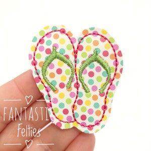 May include: A pair of white felt flip flops with a pink, green, and yellow polka dot pattern. The flip flops are embroidered with green straps.