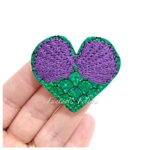May include: A purple felt heart with green glitter scales. The heart is a felt applique for crafts and sewing projects.