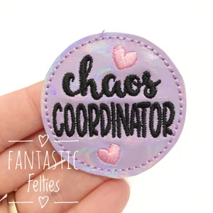 May include: A purple iridescent fabric patch with black embroidery that reads "chaos coordinator" and two pink embroidered hearts.