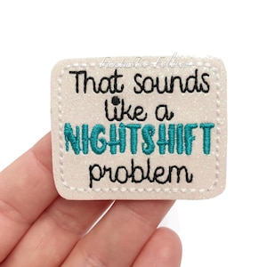 May include: A glittery, off-white square patch with the text "That sounds like a NIGHTSHIFT problem" in black and teal embroidery. The patch has a stitched border and the brand name "Fantastic Felties" is visible.