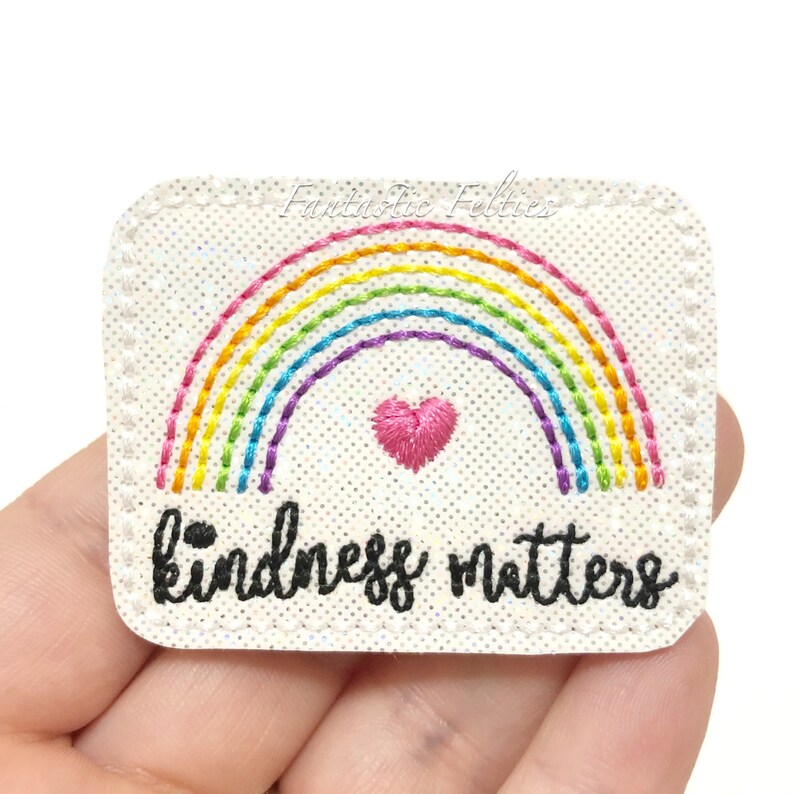 May include: White felt patch with a rainbow and a pink heart embroidered on it. The text "kindness matters" is embroidered below the rainbow.