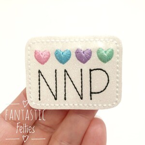 May include: White felt patch with a black stitched border and the word "NNP" in black thread. Four small hearts in pink, blue, purple, and green are stitched above the word.