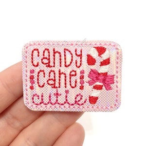 May include: Pink felt patch with red and white embroidery. The patch says "Candy Cane Cutie" with a candy cane graphic.