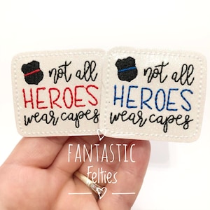 May include: Two white felt patches with black outlines. The left patch has a red and black badge with the text "not all HEROES wear capes". The right patch has a blue and black badge with the text "not all HEROES wear capes".