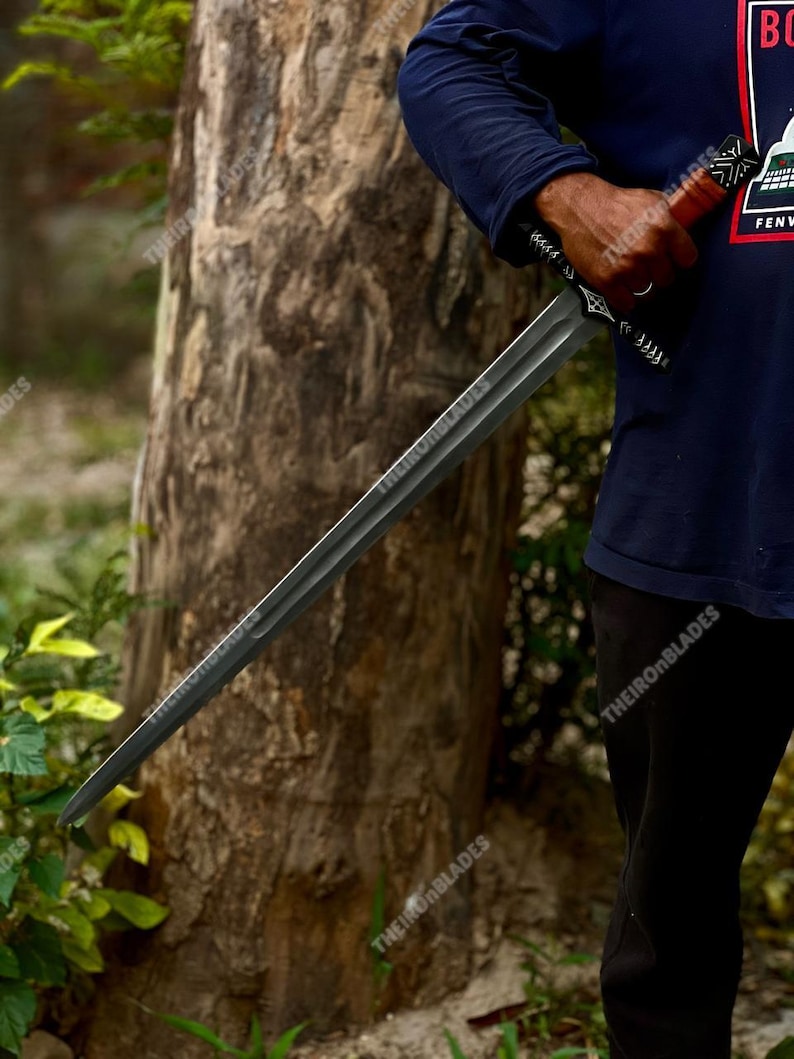 May include: A long, dark gray sword with a detailed handle and a straight blade. The sword is held in front of a tree, with the text "THEIRONBLADES" visible on the blade and handle.