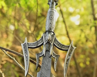 May include: A detailed close-up of a decorative sword with an ornate handle and blade. The sword features a silver-coloured metal design with intricate patterns and a green gem at the top. The blade has a unique, textured pattern.