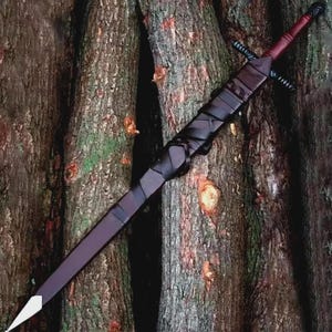 May include: A long, dark burgundy sword with a white tip, black crossguard, and a wrapped black handle. The sword is displayed against a backdrop of textured tree trunks, showcasing its craftsmanship and design.
