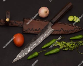 May include: A forged steel kitchen knife with a dark wooden handle and a wavy hamon line on the blade, accompanied by a brown leather sheath with a brass button closure. The knife is displayed alongside a tomato, onion, and green chilies.