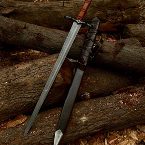 May include: A long, silver sword with a brown leather-wrapped handle and a black crossguard. The sword is sheathed in a black leather scabbard with a silver tip. The sword and scabbard are resting on a pile of wooden logs.