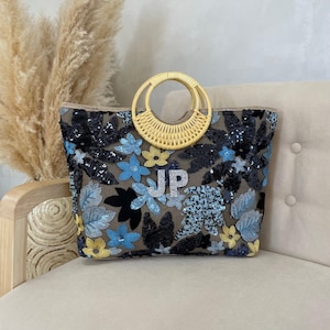 May include: A rectangular tote bag with a woven bamboo handle. The bag is decorated with blue, yellow, and black floral sequins. The initials "JP" are embroidered on the front of the bag.
