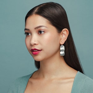 May include: A woman with long dark hair wearing a teal sweater and silver earrings with a wavy texture.