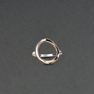 Può includere: Un anello d'argento con una fascia ovale in oro rosa. La fascia è aperta e ha una forma liscia e organica.