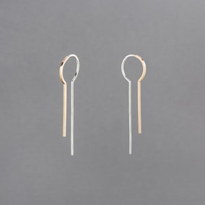 Puede incluir: Un par de pendientes con un diseño en oro y plata. Los pendientes están hechos de metal fino y tienen un estilo simple y minimalista.