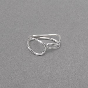 May include: A silver ring featuring a distinctive, abstract design. The ring is crafted from two interwoven bands, one of which creates a circle.