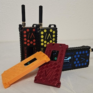 May include: A collection of black, red, and yellow electronic devices with antennas. The devices have a honeycomb pattern and the text "MESTASTIC" is visible. There are also orange and red covers.