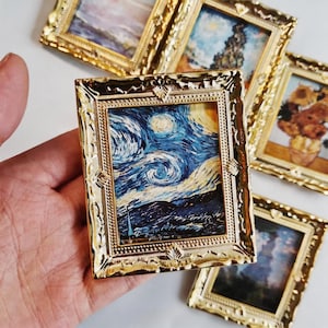 May include: A miniature rectangular painting featuring a reproduction of The Starry Night, encased in an ornate, shiny gold-colored frame with intricate embossed detailing along the edges and corners, held in a vertical orientation.
